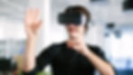 Man in black shirt wearing VR headset, gesturing with hands in a modern office. Bright, relaxed setting, no visible text.