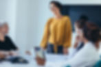 a person in front of a room talking to a table of people